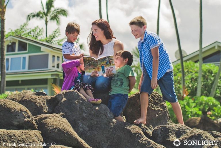 a mom reading outdoors with three children who are smiling as the moom reads the book.