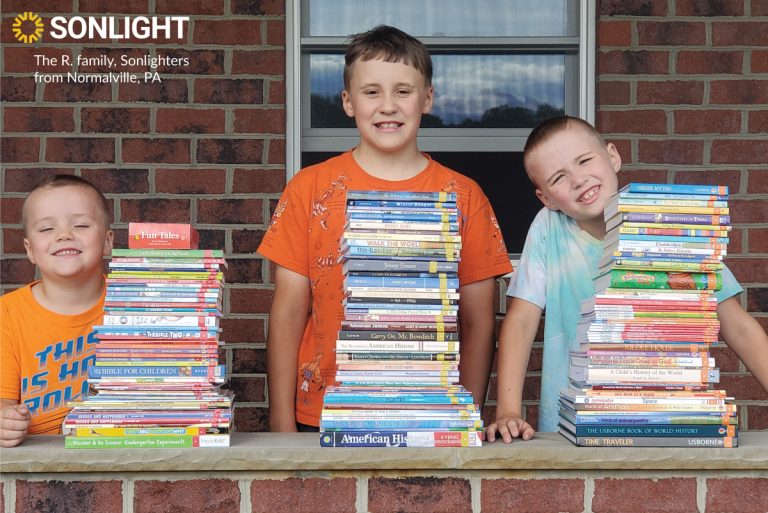 three children pose behind brick wall with Sonlight stacks