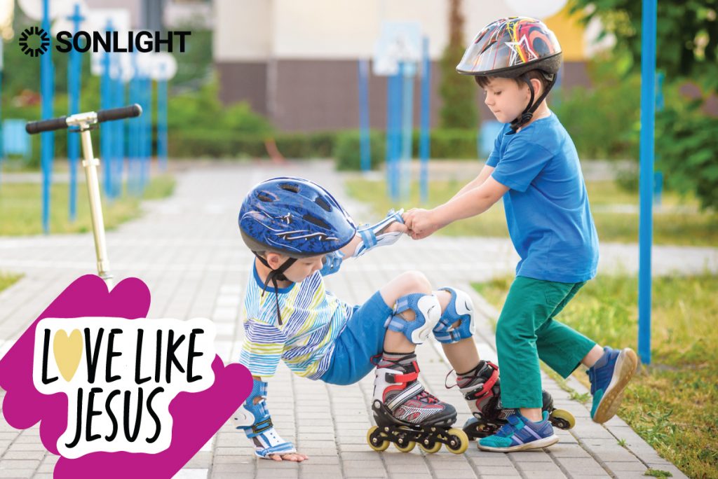 Two boys, one helping the other up from the ground, with the text "LOVE LIKE JESUS" 