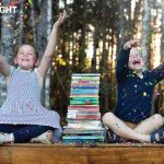 two children sit on either side of a stack of books